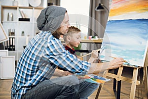 Schoolboy and his teacher drawing together on easel