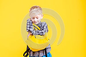 Schoolboy holding backpack  on yellow