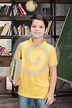 Schoolboy holding books while standing near chalkboard