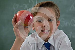Schoolboy holding red apple against chalkboard