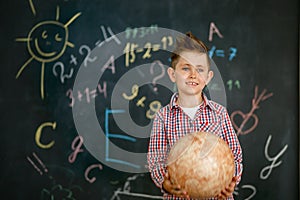 A schoolboy holding a round globe in the hands of a chalkboard painted with a chalkboard