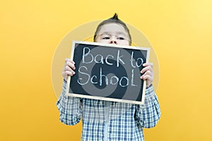 Schoolboy holding a tablet in his hands with the inscription Back to school on a yellow background