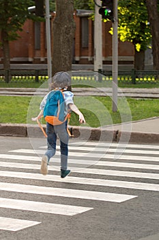 Schoolboy with a knapsack behind his back runs across the road a