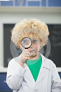 Schoolboy in lab coat holding magnifying glass
