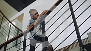 Schoolboy leaning stairs railing looking corridor. Boy standing stairway alone.