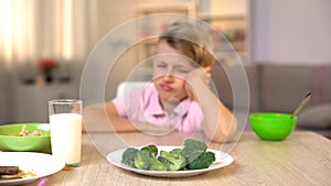 Schoolboy looking sadly at broccoli on white plate, childhood nutrition, food