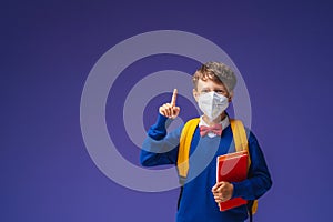 Schoolboy in mask, in uniform with book and backpack on purple background