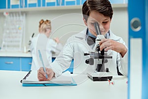 Schoolboy with microscope and copybook in science laboratory