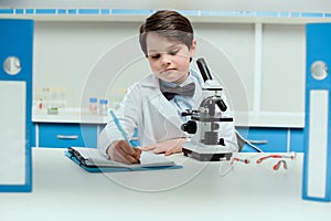 Schoolboy with microscope and copybook in science laboratory