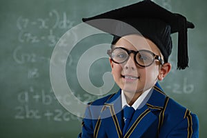 Schoolboy in mortar board standing against chalkboard