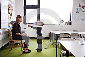 Schoolboy at primary school presenting a gift to his female teacher in a classroom, full length, side view