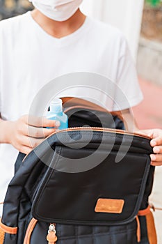 Schoolboy puts sanitizer and mask into her backpack. Student safety after covid-19 pandemic. Back to school after coronavirus