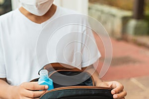 Schoolboy puts sanitizer and mask into her backpack. Student safety after covid-19 pandemic. Back to school after coronavirus