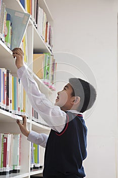 Schoolboy reaching for book off bookshelf