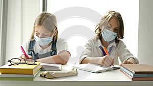 Schoolboy and a schoolgirl are sitting at the same desk in a lesson. On the faces of adolescents, protective masks