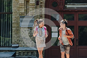 Schoolboy and schoolgirl smiling and looking at each other while running in schoolyard