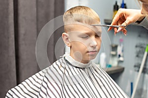 A schoolboy is sitting in a barbershop, doing his hair with scissors for haircuts