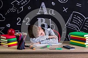 Schoolboy sleeping at the desk with a head leaned on the hands, surrounded with school supplies. Chalkboard as a