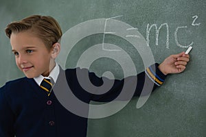 Schoolboy solving maths formula on chalkboard