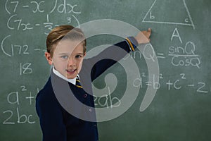 Schoolboy solving maths formula on chalkboard