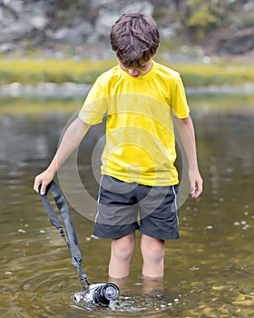 A schoolboy stands in the river on outdooor and destroys a mirrorless photo camera