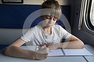 Schoolboy at table in compartment train. Teaching child while traveling