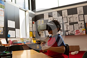 Schoolboy using virtual reality headset at desk in a classroom