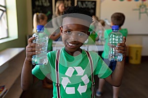 Schoolboy wearing a green t shirt with a white recycling logo on it and holding two plastic water bo