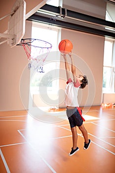 Schoolboy wearing sport clothing throwing ball into basket