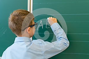 schoolboy writes the letters A,B,and C in chalk on a green blackboard.