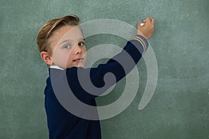 Schoolboy writing with chalk on chalkboard