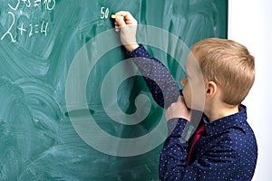 Schoolboy writing on chalkboard in classroom