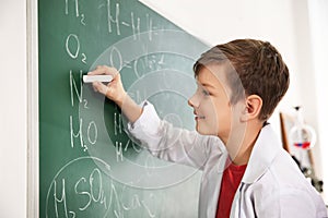 Schoolboy writing chemical formulas on chalkboard