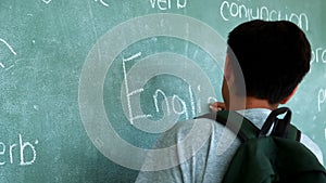 Schoolboy writing english word on chalkboard in classroom