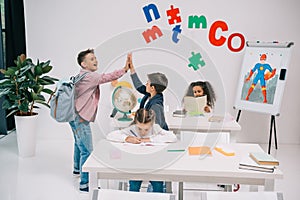 Schoolboys giving high five while schoolgirls studying in classroom