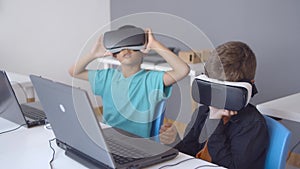 Schoolboys wearing VR headset sitting at desk with laptop