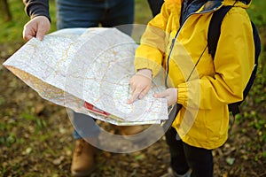 Schoolchild and his mature father hiking together and exploring nature. Little boy with dad looking map during orienteering in