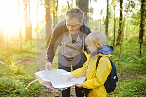 Schoolchild and his mature father hiking together and exploring nature. Little boy with dad looking map during orienteering in