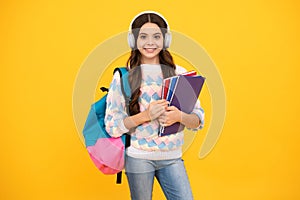 Schoolchild, teenage student girl with headphones and school bag backpack on yellow isolated studio background. Children