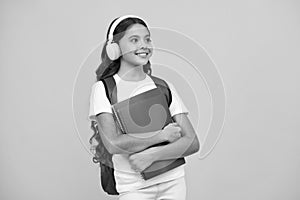 Schoolchild, teenage student girl with headphones and school bag backpack on yellow  studio background. Children