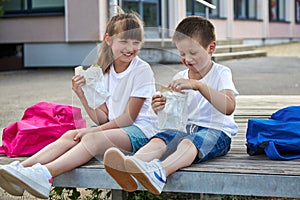 Schoolchildren boy and girl laugh and eat their lunch, snack, breakfast in the school yard. Food for children in educational