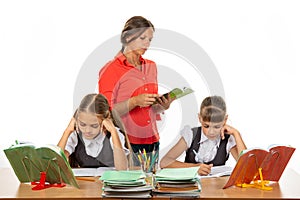 Schoolchildren at the desk do the assignment, the teacher in the background reads the assignment