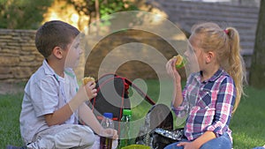 Schoolchildren eat sandwiches and talk during lunch time sitting on lawn in schoolyard close up