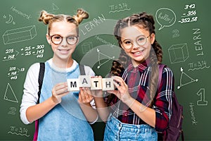 schoolchildren holding wooden cubes with word math near blackboard photo