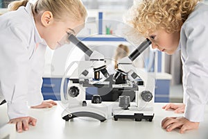 Schoolchildren in lab coats using microscopes