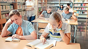 Schoolchildren preparing for lesson in school library, reading textbooks