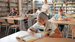 Schoolchildren preparing for lesson in school library, reading textbooks