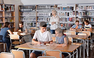 Schoolchildren preparing for lesson in school library, reading and writing