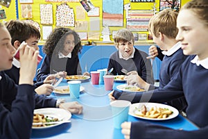 Schoolchildren Sitting At Table Eating Cooked Lunch