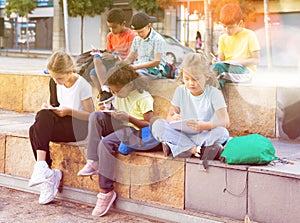Schoolchildren sitting with workbooks in schoolyard in autumn day